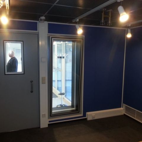 Blaue Studiowand mit schalldämmender Tür links und Schallschutzfenster rechts