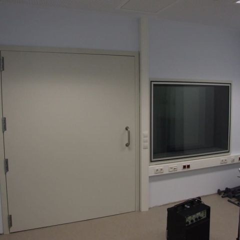 Helle Studiowand mit Schallschutzfenster rechts und schalldämmender Tür links