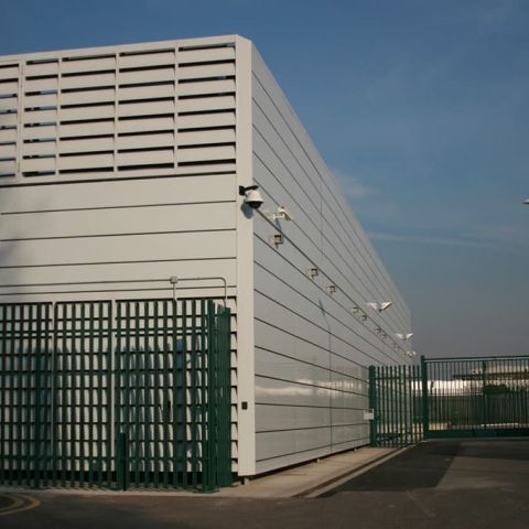 Weißer Fassaden-Schallschutz an Gebäude mit grünem Zaun daneben