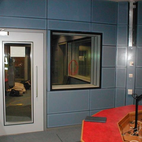 Blaue Studiowand mit Schallschutzfenster rechts und schalldämmender Tür links
