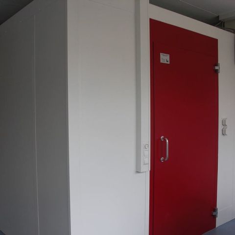 Außenansicht einer doppelwandigen weißen Hörprüfkabine mit roter Tür